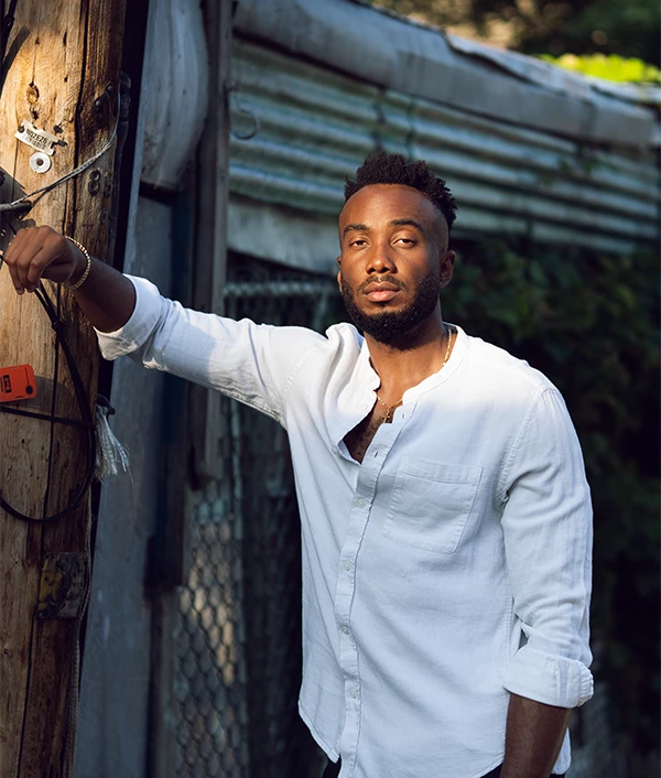 Al Faso in a white linen shirt leaning on a wooden post